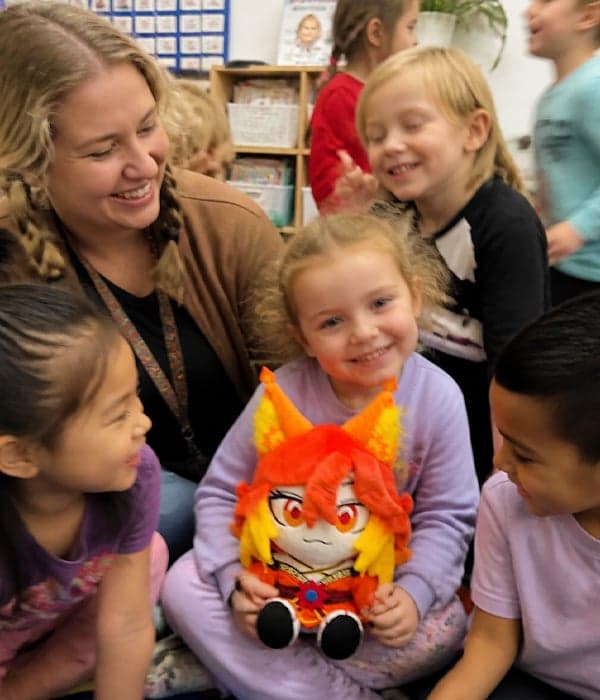 Schoolchildren in a classroom gathered around a custom red-haired anime fire character plush toy