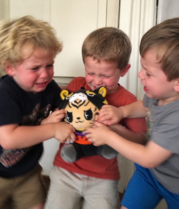Three young boys playing with a custom black-and-yellow anime tiger character plush toy