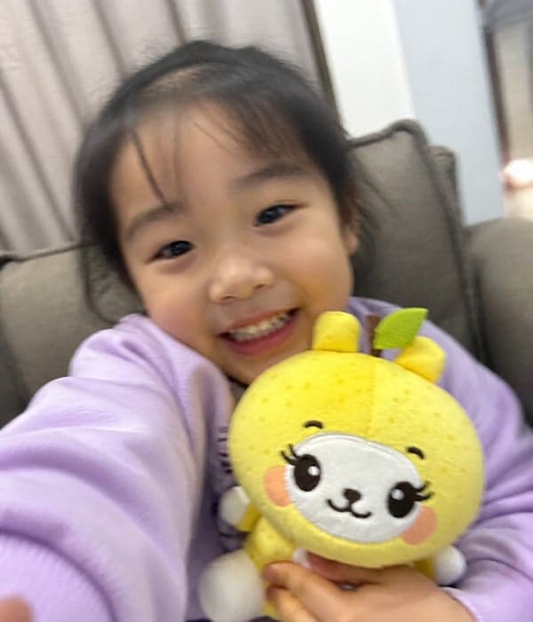 Smiling young girl holding a custom yellow bunny character plush toy with embroidered face by StarDream Toys