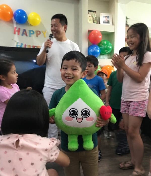 Smiling boy celebrating his birthday with a custom green leaf-shaped mascot character plush toy
